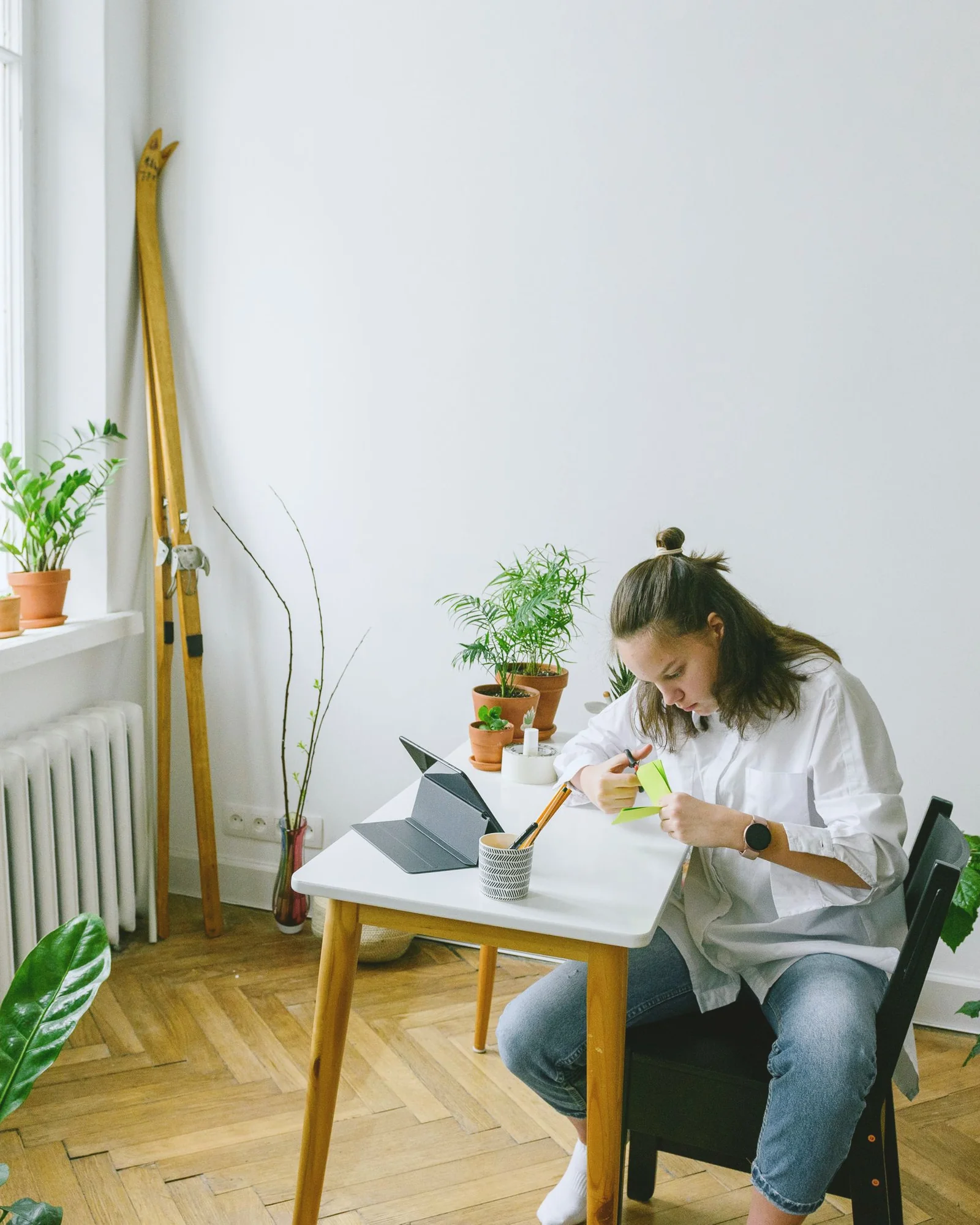 IMG P09 new italian Young woman at a small white desk cutting paper, plants and a radiator, herringbone parquet.