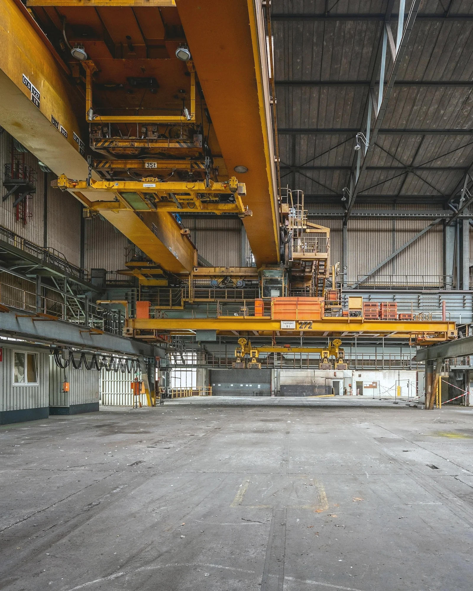 IMG S11 manifattura su Grande capannone industriale con carriponte gialli sopra un pavimento in cemento vuoto.
