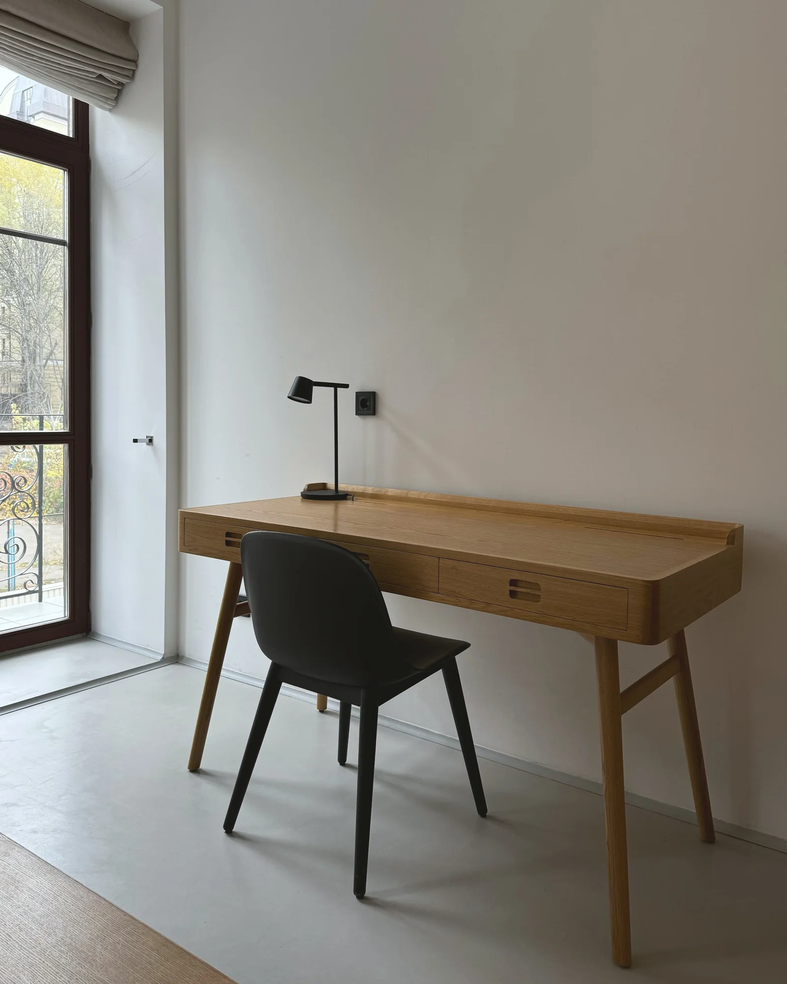 IMG S12 software e servizi Scrivania in rovere con sedia nera e piccola lampada in una stanza bianca accanto a una finestra alta.